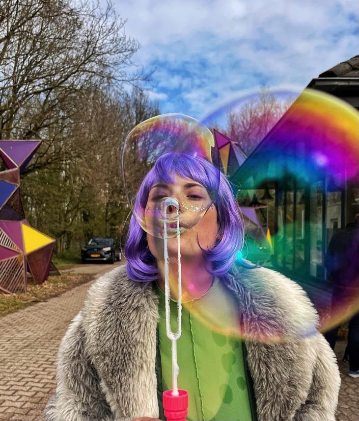 Chiara met paarse pruik blaast een reusachtige zeepbel
