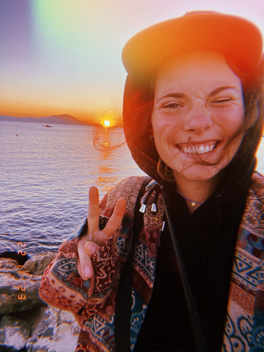 Portret van Chiara: lachend met peace-teken bij zonsondergang aan zee