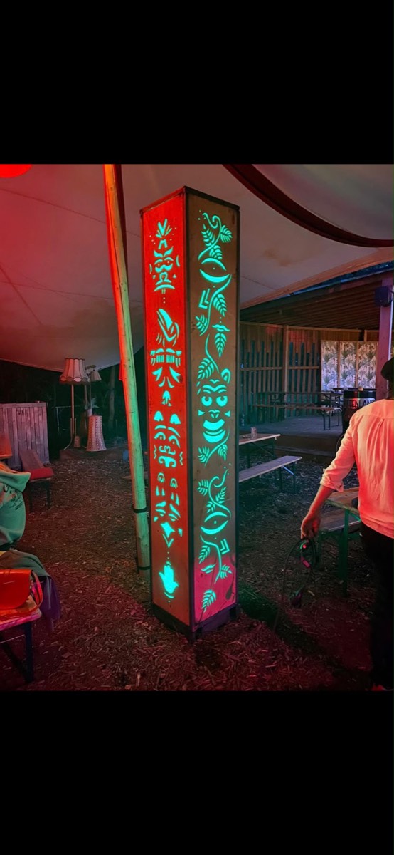 Houten lichtzuil met uitgesneden figuren, verlicht in rood en turquoise