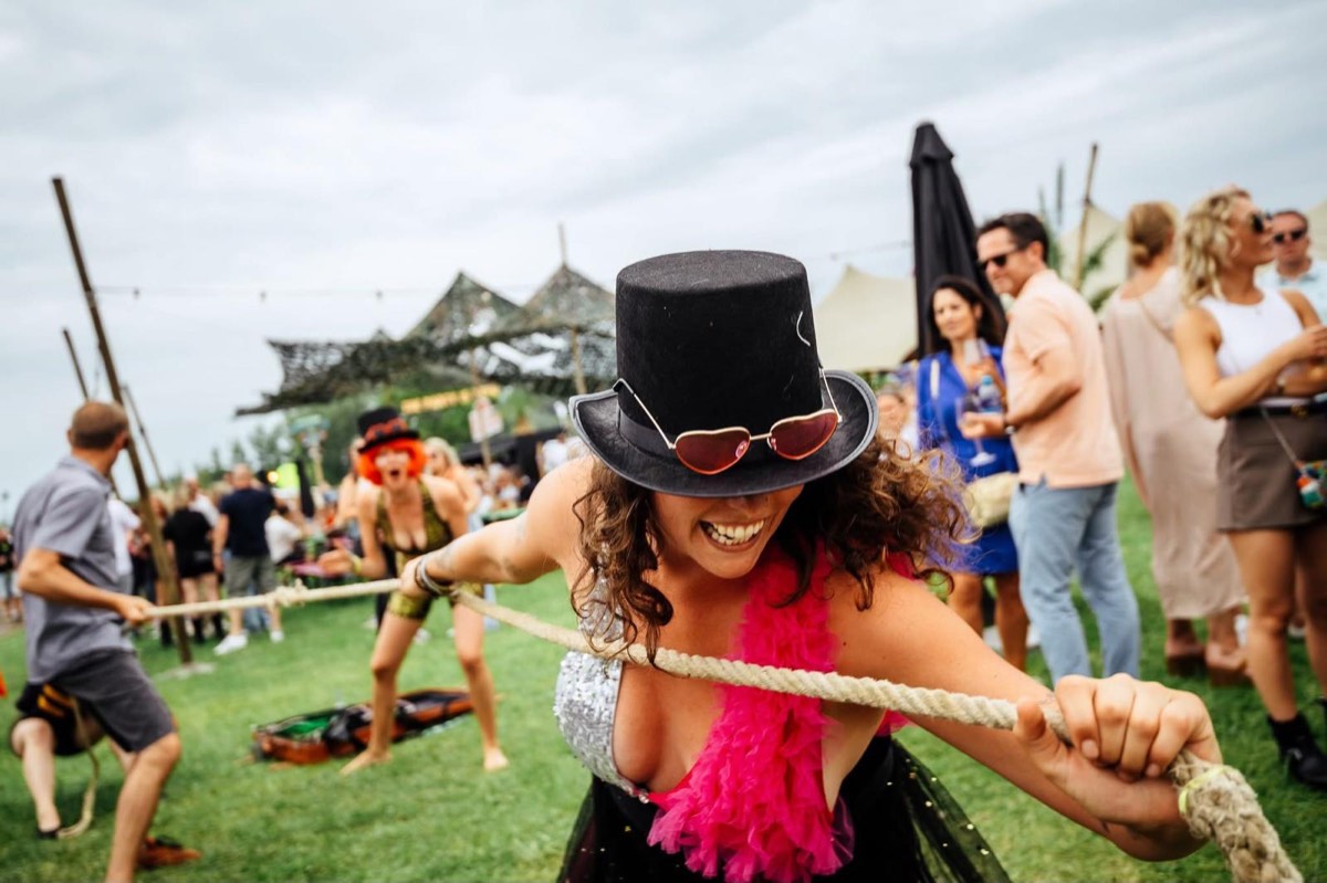 Chiara met hoge hoed en roze boa trekt lachend aan een touw tijdens een festivalspel