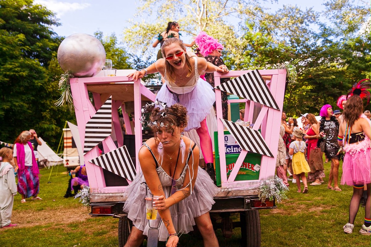 Roze paradewagen met zwart-witte vlakken, spiegelbol en performers in tule rokken